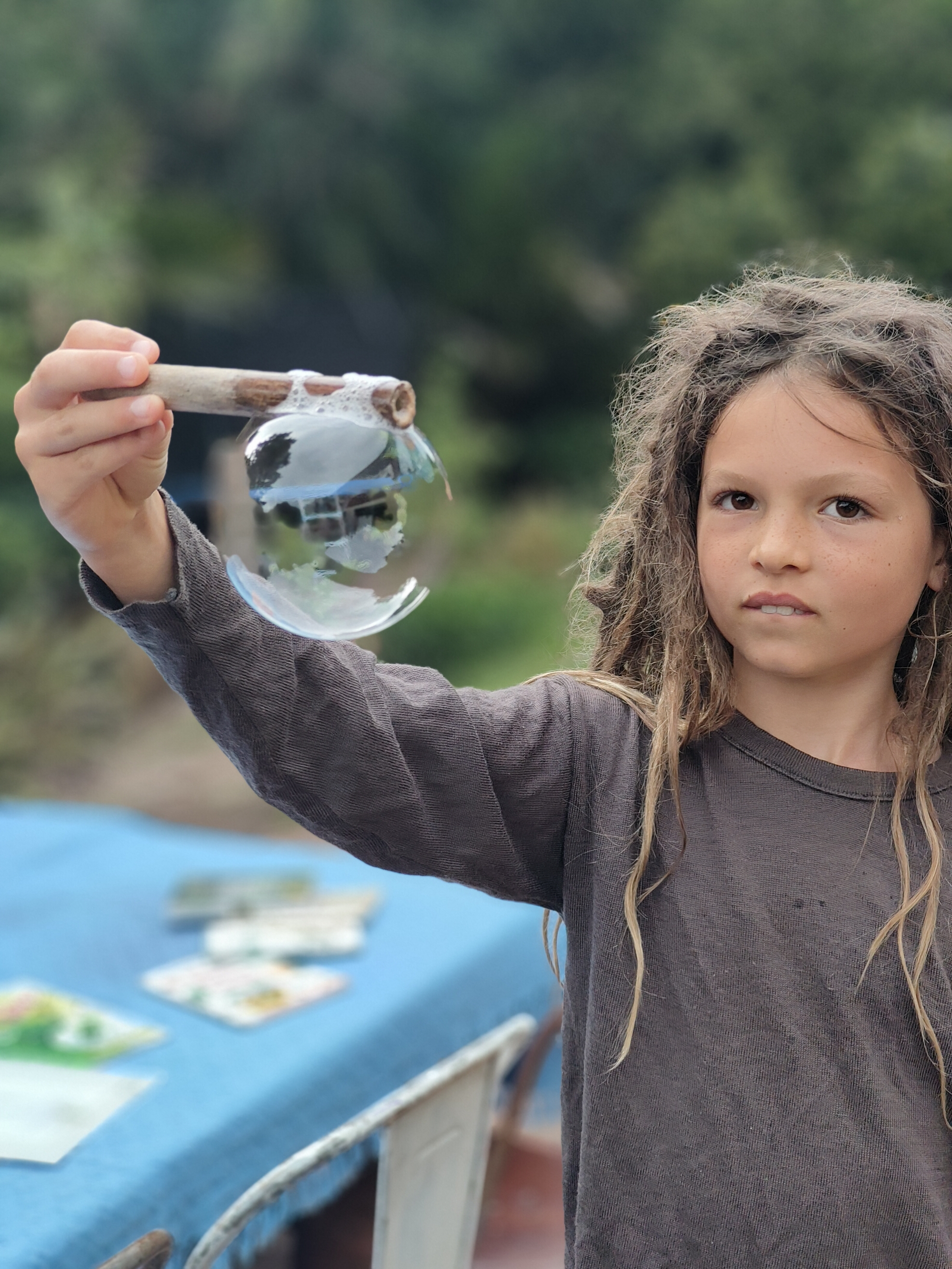 Child holding a giant soap bubble on a natural stick