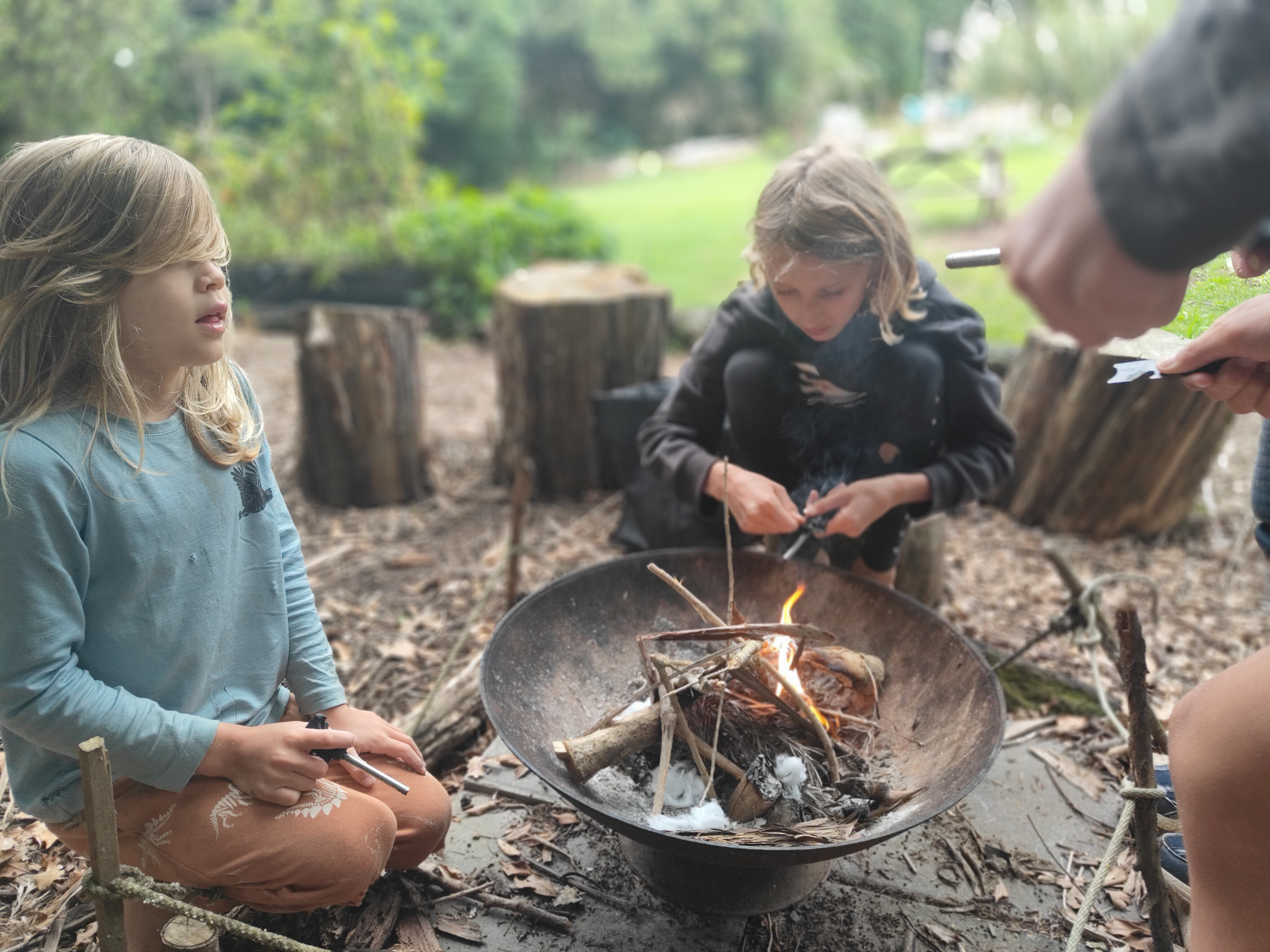 Children gathered around the fire bowl learning fire skills